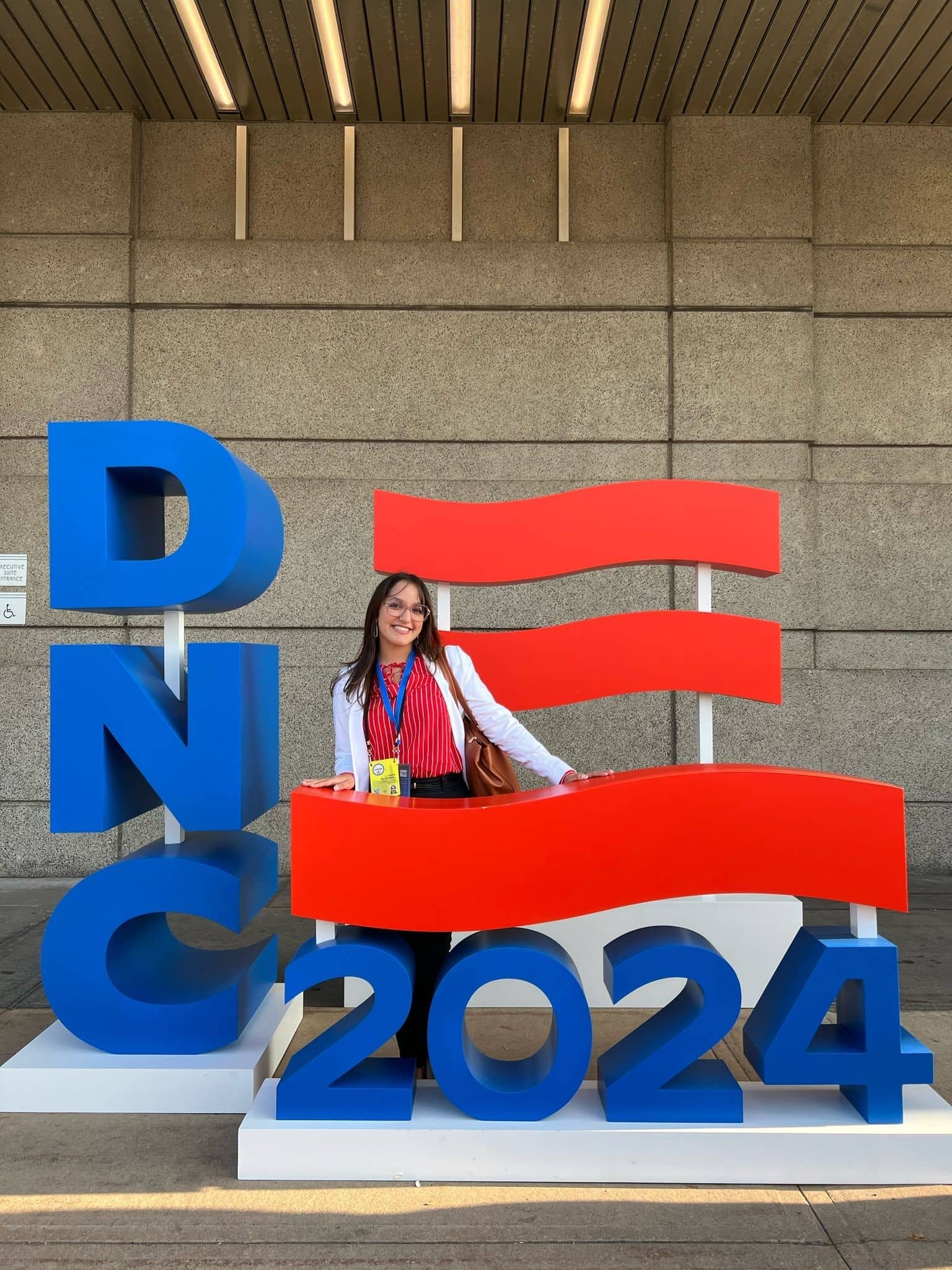 Maria Villarroel standing in front of a DNC 2024 sign at an event venue